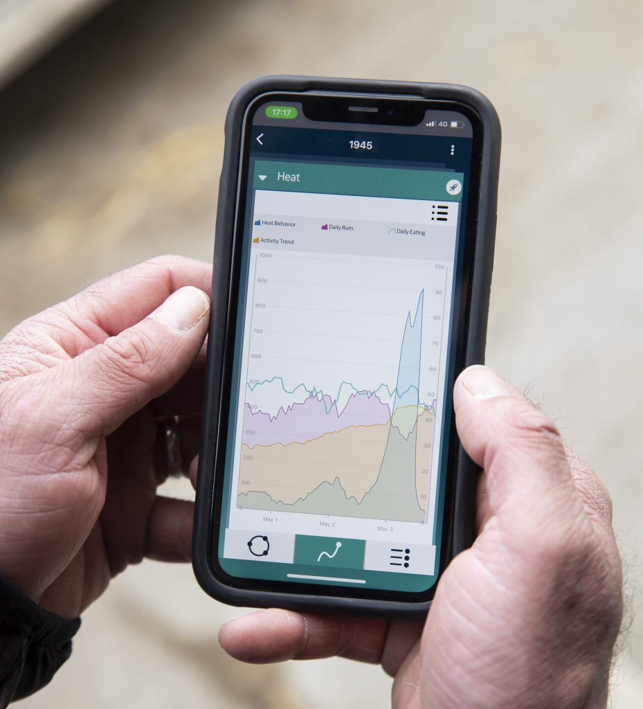 A man is holding a phone with data in graphics showing on its screen.